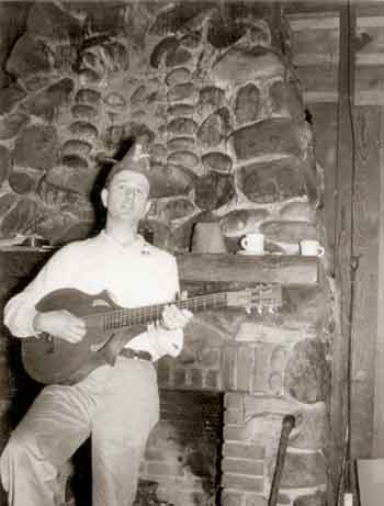 Ralph Lutz playing a lute in front of the stone fireplace.